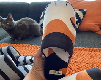 May include: A pair of black, white, and orange cat paw slippers. The slippers have a black and white striped pattern on the top and a white paw print on the toe. The slippers are made of soft, comfortable fabric and have a non-slip sole.