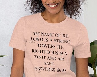 May include: A pink heather t-shirt with black text that reads "The name of the Lord is a strong tower; the righteous run to it and are safe. Proverbs 18:10"