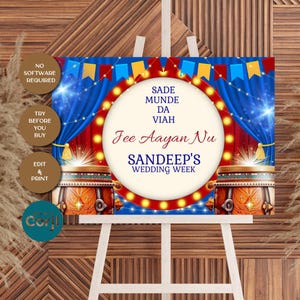 May include: A wedding sign on an easel with a festive design. The sign features text in a circular frame with a red and yellow light border. The background includes blue curtains, decorative drums, and text that reads "Sandeep's Wedding Week."
