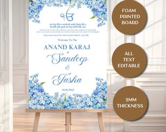 May include: A wedding welcome sign with blue floral accents and text. The sign reads "Welcome To The Anand Karaj of Sandeep & Tasha 10.06.2023". The sign is on a wooden easel. The sign is a foam printed board.