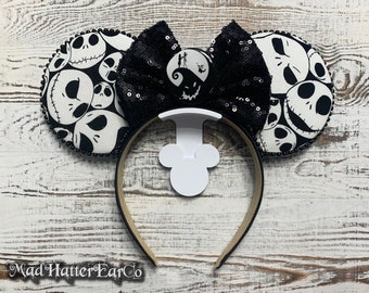 Puede incluir: Orejas de Mickey Mouse de tela en blanco y negro con un lazo de lentejuelas negras. Las orejas presentan un patrón de la cara de Jack Skellington de la película Pesadilla antes de Navidad.