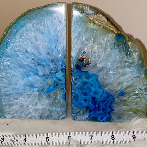 Op de afbeelding: Twee agaat boekensteunen met een opvallend blauw-wit patroon. De natuursteen heeft een gepolijst oppervlak en een ruwe, getextureerde rand. De boekensteunen zijn ongeveer 10 cm breed.