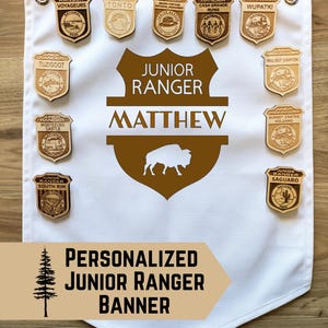 May include: A white banner with a personalized design for a Junior Ranger. The banner features wooden badges, the text "Junior Ranger Matthew", and a bison silhouette. The bottom of the banner reads "Personalized Junior Ranger Banner".