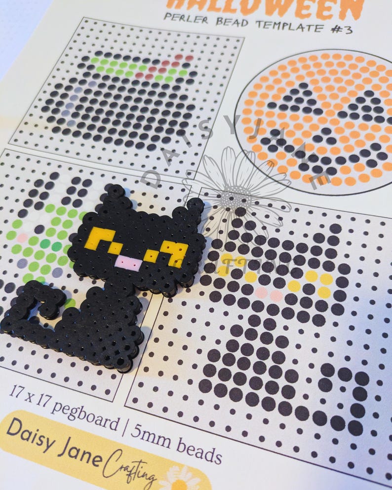 May include: A black cat figure made of fused plastic beads with yellow eyes and a pink nose, placed on a printed paper Halloween perler bead template. The template shows a 17 x 17 pegboard grid and specifies 5mm beads for the crafting project.