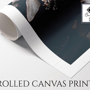 May include: A rolled canvas print featuring a dark floral image with muted tones. The white border of the canvas is visible as it curls upwards. A square logo in the top right corner contains the text Canvas Art Store. The text ROLLED CANVAS PRINT appears below.