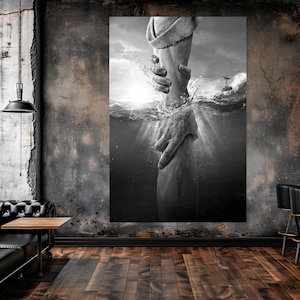 May include: Black and white art print depicting a hand reaching out of water to grasp another hand. The image captures a moment of rescue or connection, with light rays shining through the water. The artwork is displayed in a room with a black leather sofa and a wooden floor.