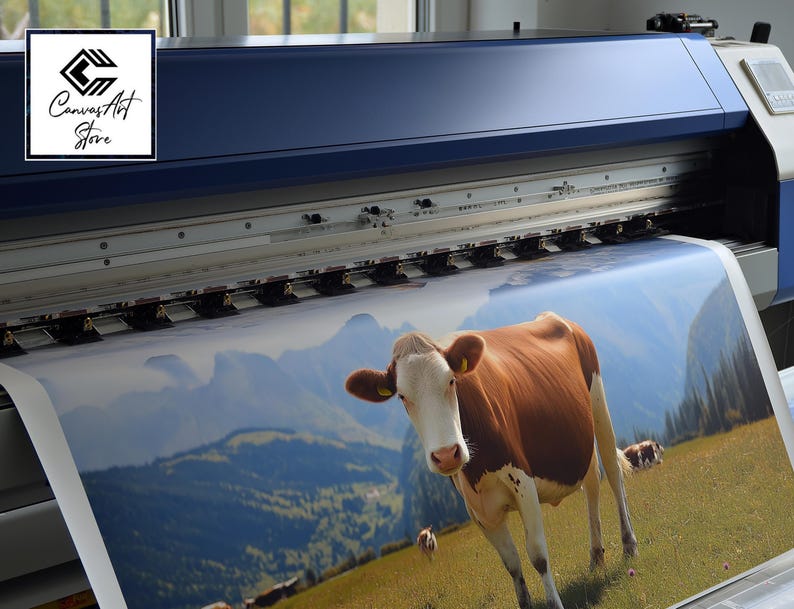 May include: A large-format industrial printer outputting a high-resolution print of a brown and white cow standing in a grassy mountain meadow. The printer features a dark blue casing and a logo reading Canvas Art Store in the upper left corner.