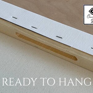 May include: A wooden canvas stretcher bar frame with white canvas fabric pulled taut and secured with metal staples along the edge. The frame features a recessed slot and the text READY TO HANG is printed below. A logo for Canvas Art Store is visible.