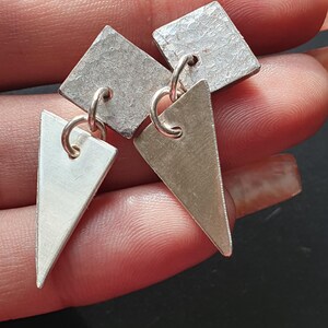May include: A pair of silver earrings with geometric shapes. One earring has a square and a triangle, the other has two triangles.