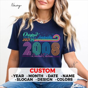 Peut inclure: Un t-shirt bleu marine à manches courtes avec un motif coloré portant le texte Original Since July 25th Isabella 2008 Limited Edition. Le design présente des lignes courbes de style rétro et une texture vieillie en rose, orange et bleu.