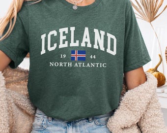 May include: Dark green t-shirt with the word "ICELAND" in white block letters. Below the word "ICELAND" is a small rectangle with the Icelandic flag and the numbers "19" and "44". The words "NORTH ATLANTIC" are below the flag. The words "Heather Forest" are in the upper left corner.