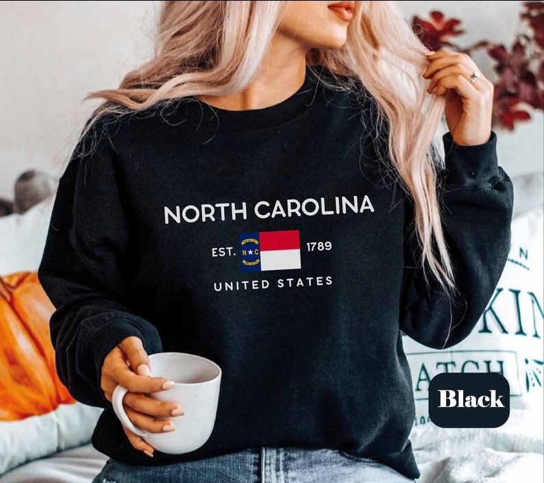 May include: Black sweatshirt with a white graphic of the North Carolina state flag and the text "NORTH CAROLINA EST. 1789 UNITED STATES".