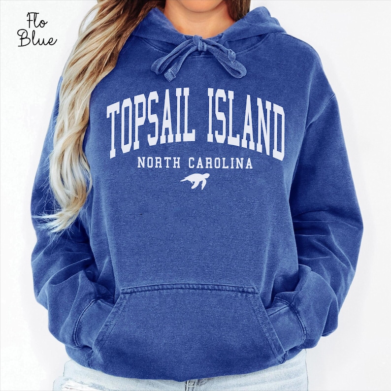 May include: A blue hooded sweatshirt with the text "TOPSAIL ISLAND NORTH CAROLINA" in white block letters. A turtle graphic is below the text. The sweatshirt has a front pocket and a drawstring hood.