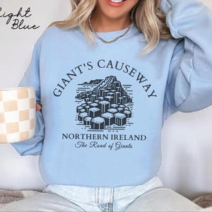 May include: Light blue sweatshirt with a black graphic of the Giant's Causeway in Northern Ireland. The text "Giant's Causeway" is in a black circle around the graphic. The text "Northern Ireland" and "The Road of Giants" is below the graphic.
