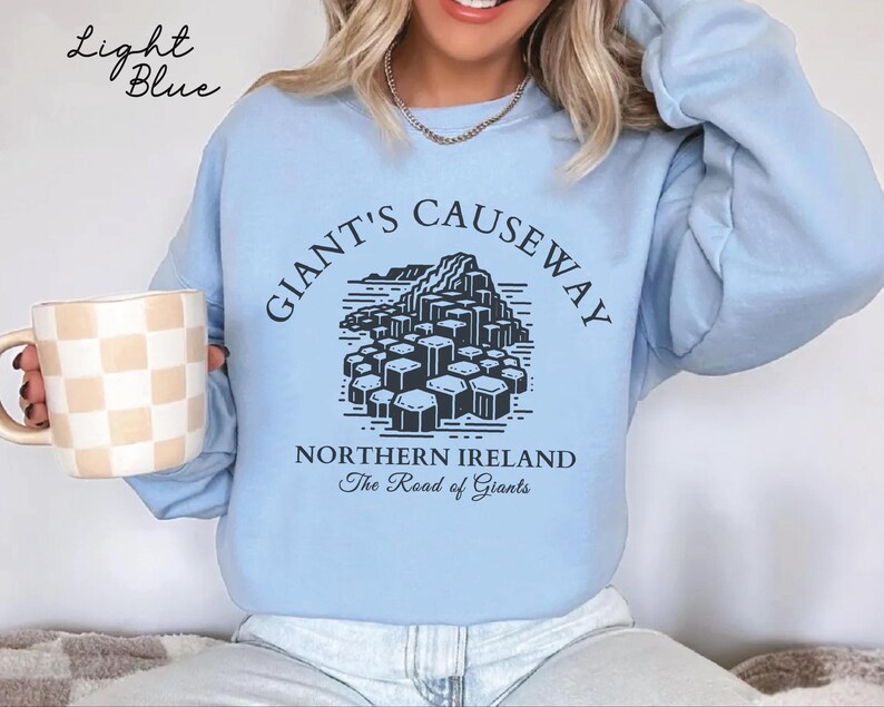May include: Light blue sweatshirt with a black graphic of the Giant's Causeway in Northern Ireland. The text "Giant's Causeway" is in a black circle around the graphic. The text "Northern Ireland" and "The Road of Giants" is below the graphic.