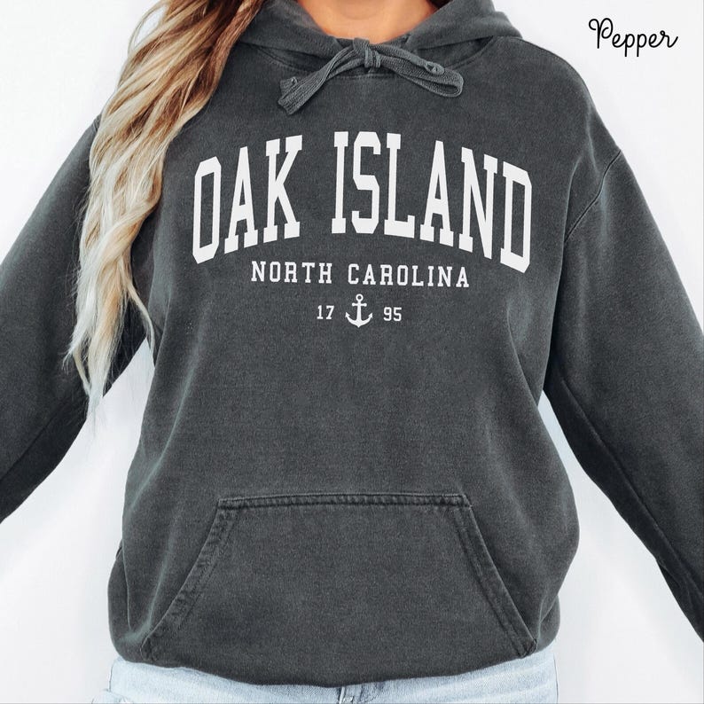 May include: Dark grey hoodie with a front pocket and drawstring. The white text on the front reads "OAK ISLAND NORTH CAROLINA" with the numbers "17 95" and an anchor graphic. The hoodie is a comfortable, casual style.