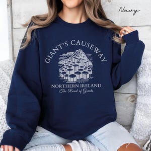May include: Navy blue sweatshirt with a white graphic of the Giant's Causeway in Northern Ireland. The text "Giant's Causeway" is in a circular arc above the graphic, and the text "Northern Ireland The Road of Giants" is below the graphic.