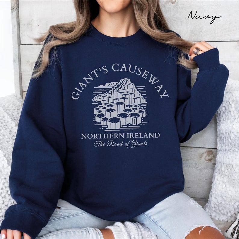 May include: Navy blue sweatshirt with a white graphic of the Giant's Causeway in Northern Ireland. The text "Giant's Causeway" is in a circular arc above the graphic, and the text "Northern Ireland The Road of Giants" is below the graphic.
