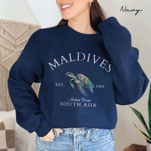 Könnte beinhalten: Ein marineblauer Pullover mit einem Aufdruck einer Meeresschildkröte und dem Text "MALDIVES EST. 1965 Indian Ocean SOUTH ASIA".