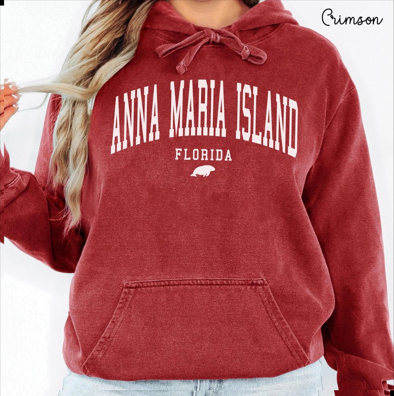 May include: Crimson red hooded sweatshirt with a front pocket and drawstring. The sweatshirt features the text "ANNA MARIA ISLAND FLORIDA" in white block letters, with a small white illustration of a sea creature below the text.