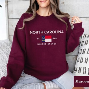 May include: Maroon sweatshirt with a white graphic of the North Carolina state flag and the text "NORTH CAROLINA EST. 1789 UNITED STATES".