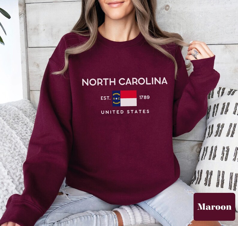 May include: Maroon sweatshirt with a white graphic of the North Carolina state flag and the text "NORTH CAROLINA EST. 1789 UNITED STATES".