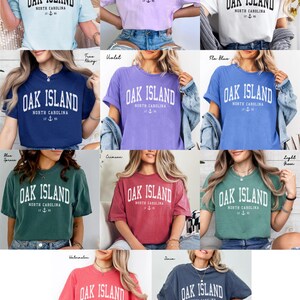 May include: A selection of short-sleeved t-shirts in diverse colours, each bearing the text "OAK ISLAND NORTH CAROLINA" in a bold, arched font. The shirts have a vintage, slightly faded look, with a nautical anchor graphic.