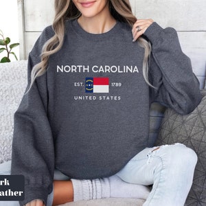 May include: Dark heather grey sweatshirt with the text "NORTH CAROLINA" and the North Carolina state flag. The text "EST. 1789" and "UNITED STATES" are also printed on the sweatshirt.