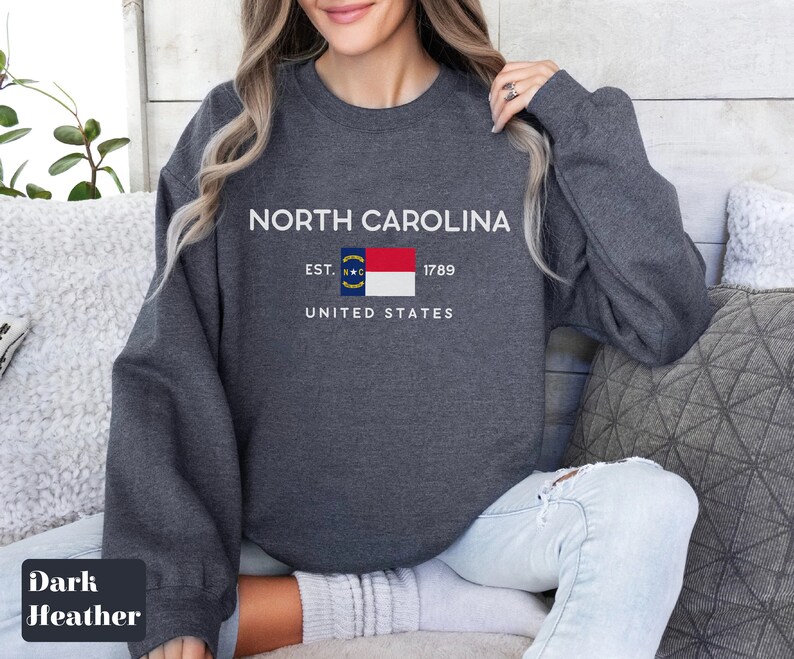 May include: Dark heather grey sweatshirt with the text "NORTH CAROLINA" and the North Carolina state flag. The text "EST. 1789" and "UNITED STATES" are also printed on the sweatshirt.