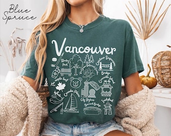 May include: A dark green short-sleeve t-shirt featuring white line art graphics of Vancouver landmarks and icons, including a hockey stick, maple leaf, bear face, sailboat, and city skyline, with text labels for each specific location and object.