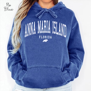 Könnte beinhalten: Ein blauer Kapuzenpullover mit dem Text "ANNA MARIA ISLAND FLORIDA" in weißen Blockbuchstaben. Der Pullover hat eine Kapuze mit Kordelzug und eine Vordertasche. Die Farbe ist ein verwaschenes Blau.