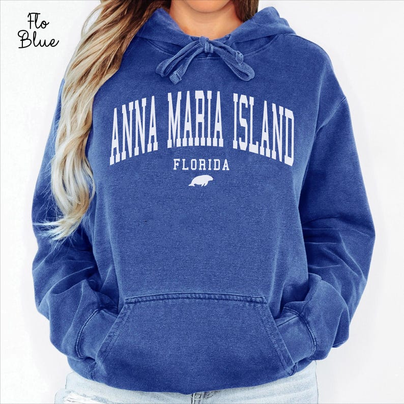 May include: A blue hooded sweatshirt with the text "ANNA MARIA ISLAND FLORIDA" in white block letters. The sweatshirt has a drawstring hood and a front pocket. The color is a faded blue.