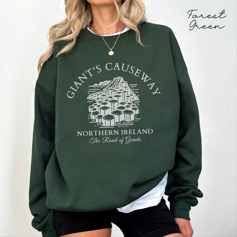 May include: Forest green sweatshirt with a white graphic print of the Giant's Causeway in Northern Ireland. The text "Giant's Causeway" is in a circular design around the graphic. The text "Northern Ireland" and "The Road of Giants" is below the graphic.