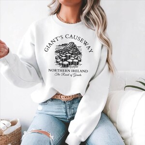 May include: White sweatshirt with a black graphic of the Giant's Causeway in Northern Ireland. The text "Giant's Causeway" is in a circle around the graphic. The text "Northern Ireland" and "The Road of Giants" are below the graphic.