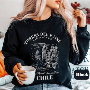 May include: Black sweatshirt featuring a white graphic of the Torres del Paine National Park in Chile. The text "TORRES DEL PAINE national park" is above the illustration. The word "CHILE" is printed below the illustration. The word "Black" is in a white box.