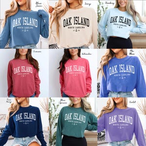 May include: A selection of long-sleeved sweatshirts in diverse colours, each featuring the white text "OAK ISLAND NORTH CAROLINA". The sweatshirts are available in hues such as blue, cream, crimson, and violet.
