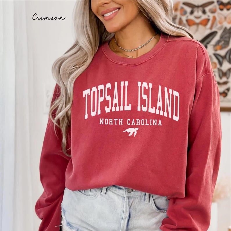 May include: Crimson red sweatshirt with the text "TOPSAIL ISLAND NORTH CAROLINA" in white block letters. A white sea turtle graphic is below the text. The sweatshirt is a crew neck style.