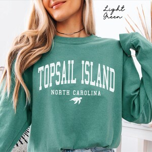 May include: Light green sweatshirt with the text "TOPSAIL ISLAND NORTH CAROLINA" in white block letters. A white turtle graphic is below the text. The words "Light Green" are written in cursive in the upper right corner.