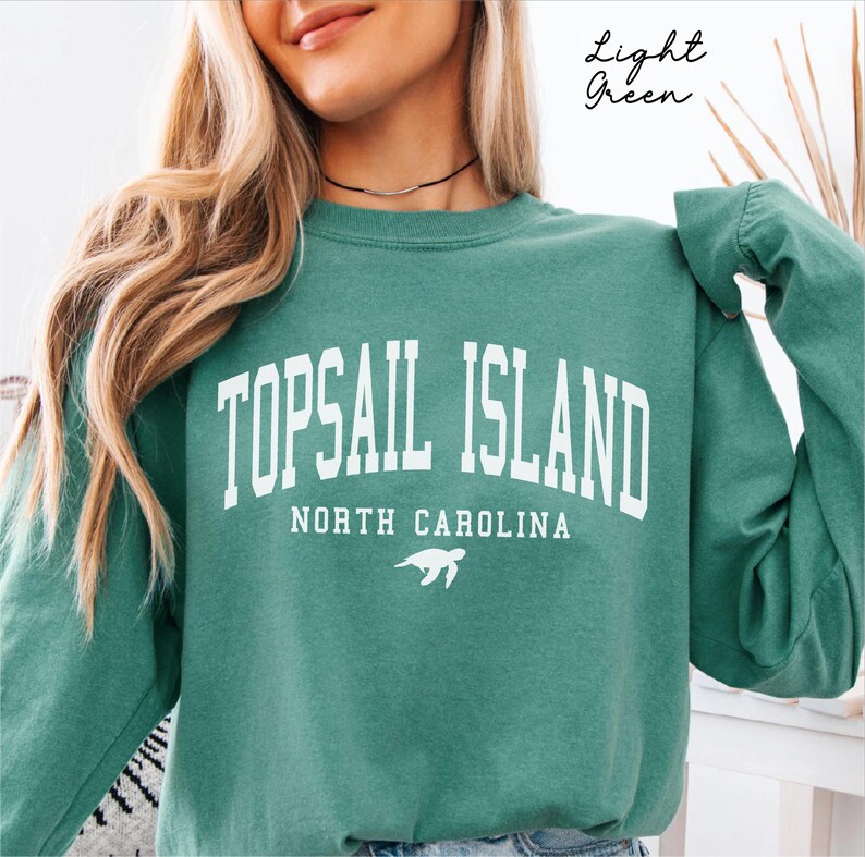 May include: Light green sweatshirt with the text "TOPSAIL ISLAND NORTH CAROLINA" in white block letters. A white turtle graphic is below the text. The words "Light Green" are written in cursive in the upper right corner.