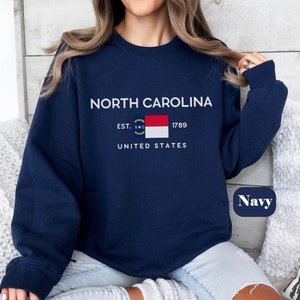 May include: Navy blue sweatshirt with white text that reads "NORTH CAROLINA EST. 1789 UNITED STATES" and a small image of the North Carolina state flag. The word "Navy" is written in white on a blue oval.