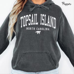 May include: Dark gray hoodie with the text "TOPSAIL ISLAND NORTH CAROLINA" in white block letters. A white turtle graphic is below the text. The hoodie has a drawstring hood and a front pocket.