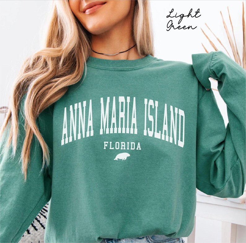 May include: Light green sweatshirt with the text "ANNA MARIA ISLAND FLORIDA" in white block letters. A small white illustration of a sea creature is below the word "FLORIDA". The words "Light Green" are written in cursive in the upper right corner.