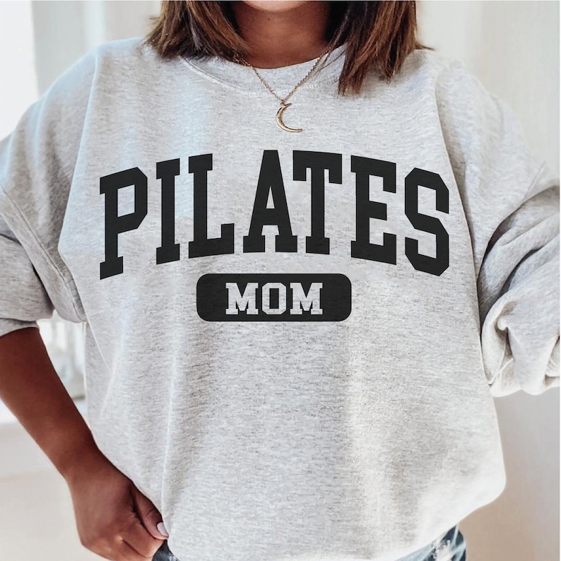 Pu&ograve; includere: Felpa grigia con testo nero che recita "PILATES MOM" in un font universitario.