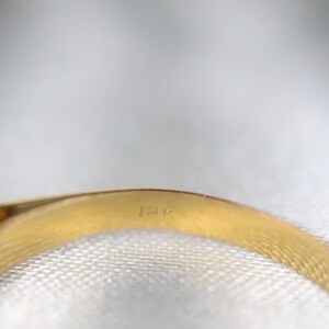 May include: A gold ring band featuring a visible hallmark stamp on the interior surface. The metal has a polished, reflective yellow gold finish, and the curved band shows a clear engraving of the characters 18K, indicating the metal purity.