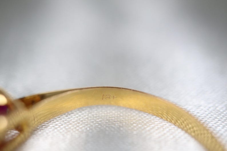 May include: A gold ring band featuring a visible hallmark stamp on the interior surface. The metal has a polished, reflective yellow gold finish, and the curved band shows a clear engraving of the characters 18K, indicating the metal purity.