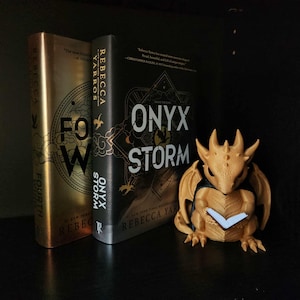 May include: A shelf display featuring two books, "Fourth Wing" and "Onyx Storm" by Rebecca Yarros, and a small, tan dragon figurine. The books have gold and black covers. The dragon figurine is holding a book.