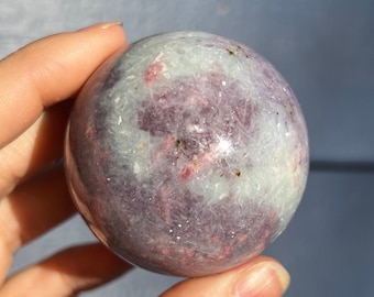 May include: A polished, white and pink sphere with red and purple flecks. The sphere is made of natural stone and has a smooth, polished surface.