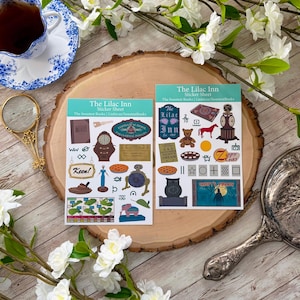 May include: Two rectangular sticker sheets titled The Lilac Inn Sticker Sheet featuring various illustrations including a grandfather clock, a teddy bear, a red horse, a pie, a blue figure, a pink elephant, an owl, and text like Keen and Zippy Gas.