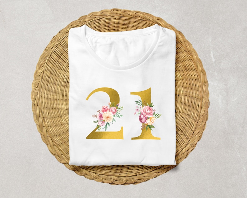 Pu&ograve; includere: Maglietta bianca con un numero 21 dorato decorato con fiori rosa e bianchi. Il numero &egrave; centrato sulla maglietta.