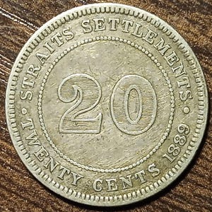 May include: A silver coin from the Straits Settlements, dated 1889, with the denomination "20 CENTS" prominently displayed. The coin's edge features a detailed pattern, and the words "STRAITS SETTLEMENTS" are inscribed around the coin's perimeter.